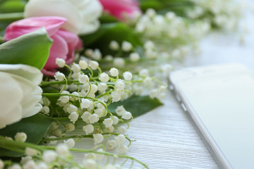 Bouquet of fresh spring flowers with smartphone on wooden background