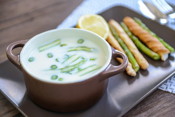 Asparagus soup with lemon and bread sticks on wooden table
