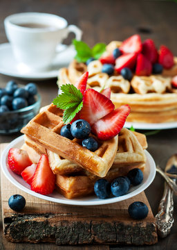 Belgian waffles with strawberries, blueberries and syrup, homemade healthy breakfast, toned image selective focus