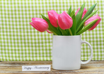 Happy Anniversary card with pink tulips in white mug on checkered background
