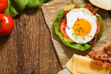 Sandwich with a fried egg, bacon, cheese and vegetables.