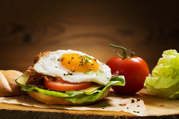 Sandwich with a fried egg, bacon, cheese and vegetables.