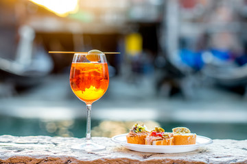 Spritz Aperol drink with venetian traditional snacks cicchetti on the water chanal background in...