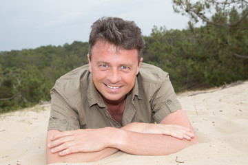 Man on beach lying in sand looking to side smiling happy wearing a green shirt.