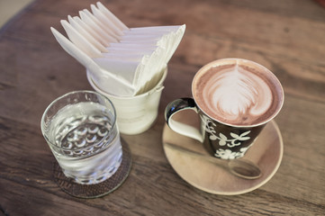 hot coffee with tissue paper coffee on wooden table coffee and glass of water coffee near red sofa