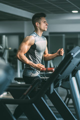 Naklejka na ściany i meble Young man in sportswear running on treadmill at gym