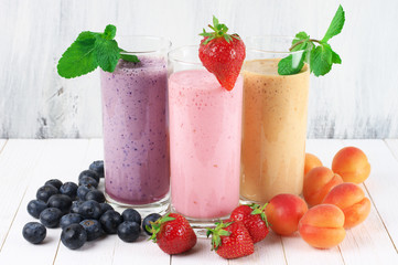 Three various protein milkshakes in glasses with fruits on rustic white wooden background.