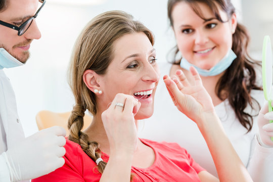 Frau beim Zahnarzt benutzt Zahnseide, der Doktor erklärt die richtige Anwendung