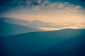 Fototapeta premium Sunrise landscape of foggy and cloudy mountain valley. Instagram toning.