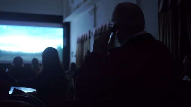 Man talking on his cell phone in dark cinema hall violating rules