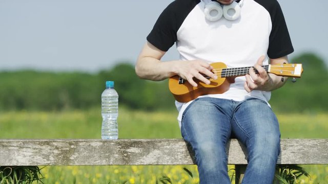 4K Static shot of unseen person playing a ukulele outdoors in a rural environment, in slow motion