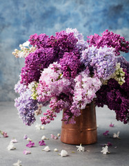 Bunch of lilac flowers in a cooper vintage jug. Blue background Copy space