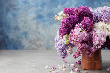 Bunch of lilac flowers in a cooper vintage jug. Blue background Copy space