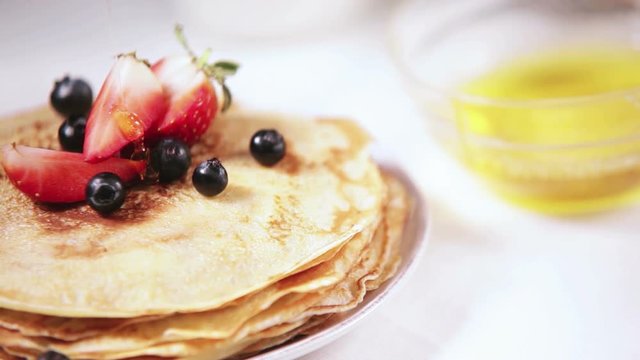 Honey dripping on just-cooked pancakes garnished with fresh fruit