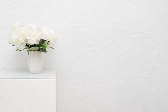 Bouquet of white peonies in ceramic vase against white stucco wall. Selective focus on the flowers.