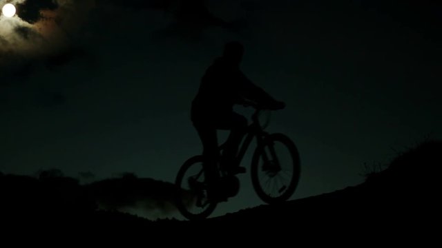 A biker rides his bicycle late in the moonlit evening
