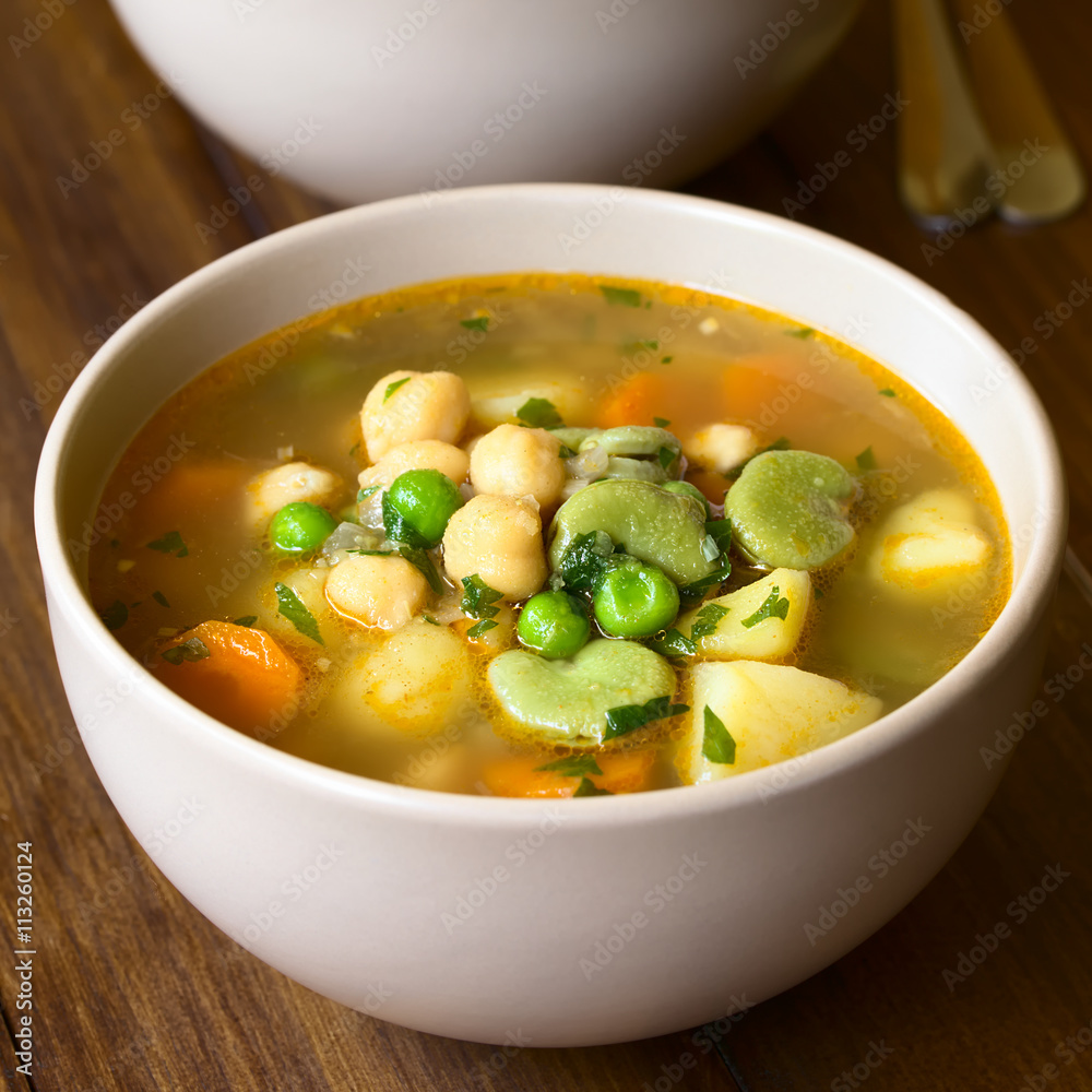 Wall mural Vegetarian chickpea soup or stew with carrot, broad bean (fava bean), pea, potato, onion, garlic and parsley, photographed on wood with natural light (Selective Focus) - Wall murals