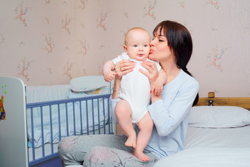 Mom pajamas tenderly kisses the baby boy on the bed in the room.