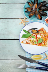 Pizza slices with seafood, red pepper and green olives on wooden table