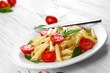 Plate of pasta with cherry tomatoes and basil leaves on table closeup