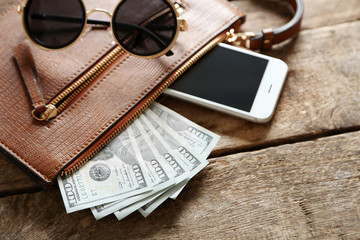 Leather purse with mobile phone, glasses and dollar banknotes on wooden table