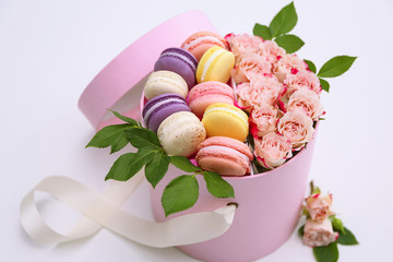 Tasty macaroons and roses in box on light background