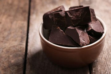 Chocolate bar pieces in a bowl on wooden background