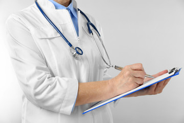 Professional doctor with clipboard on light background