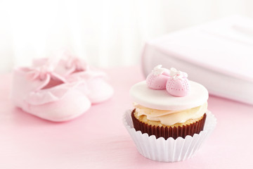 Delicious cupcake and baby shoes on bright background