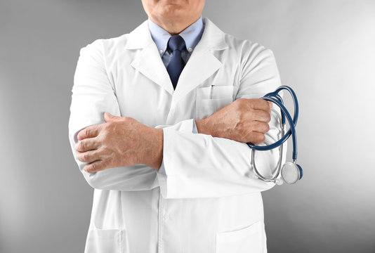 Professional doctor with stethoscope on grey background