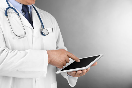 Professional doctor with tablet on grey background