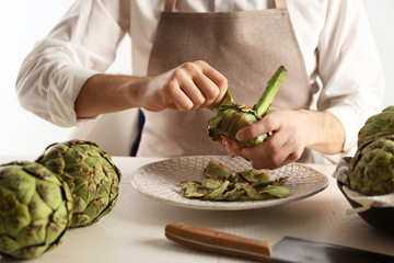 Man cooking artichokes on light background