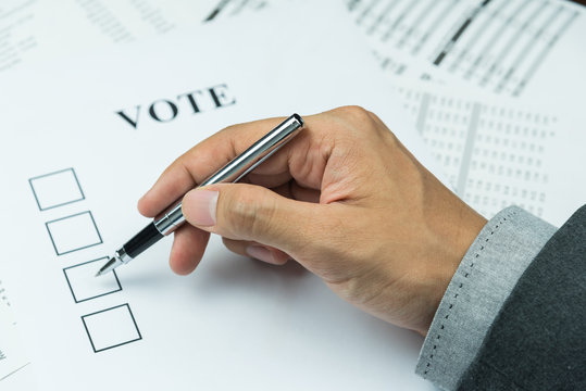 Hand of business man holding a pen trying to vote in paper