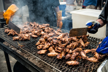 People cooking chicken wings and legs on barbecue grill street food outdoors festival
