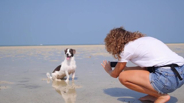 Girl Takes Picture of Dog on Beach with Smartphone on Vacation