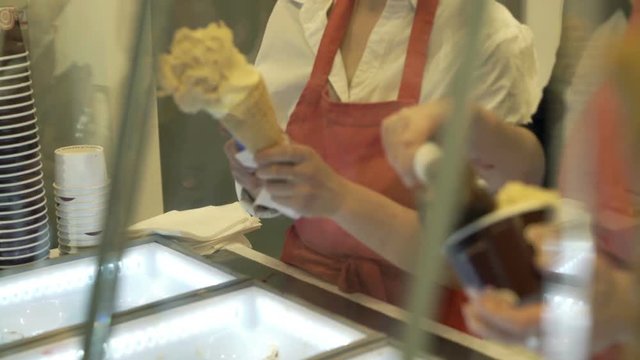 Woman put ice cream on cone in ice cream shop
