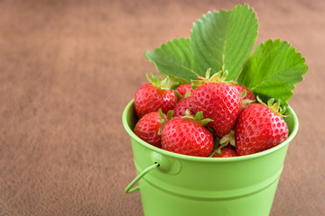 Strawberries with stems in a green bucket, along with plant leaves
