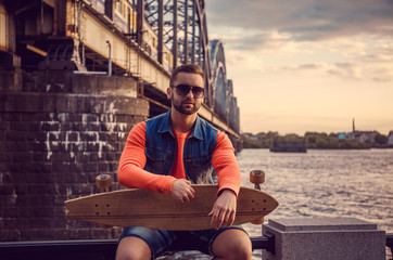 Casual male with longboard posing near river.