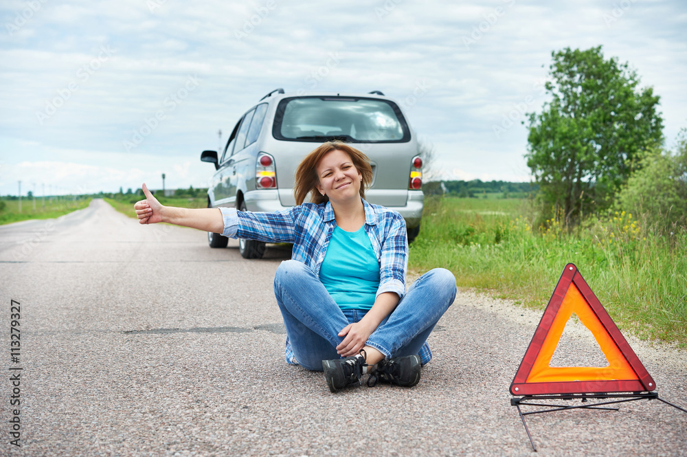 Wall mural  Woman sitting on road near emergency sign showing thumbs up