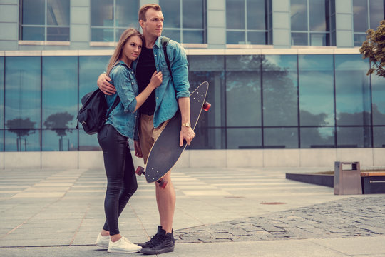 Casual couple with longboard posing on a square.