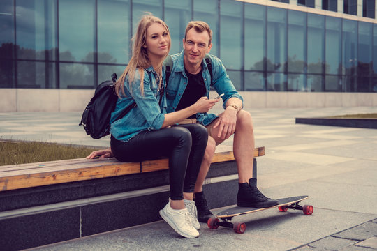 Casual couple with longboard posing on a square.