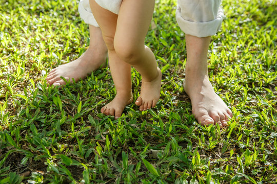 Closeup portrait of a mother helping baby to walk on grass