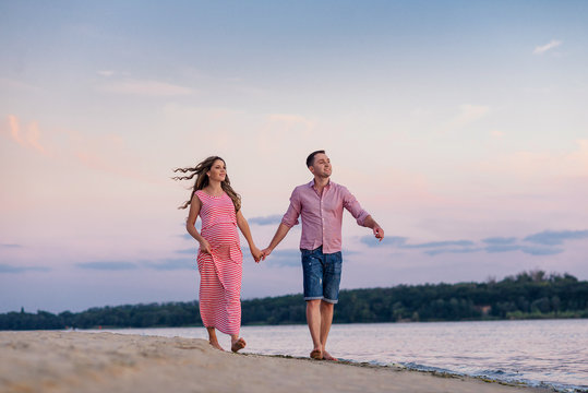 beautiful pregnant woman and her man walk on the beach on sunset