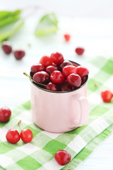 Ripe cherries in mug on a white wooden table