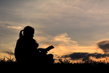 Fototapeta na wymiar Silhouette a girl reading book with teddy bear on mountain and sky sunset