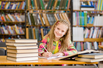 Cute little girl studying at the library and smiling