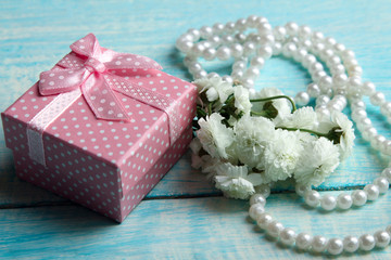 beautiful pink box with a pink ribbon near flowers on a wooden blue background with white beads