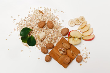 There are Banana,Apple with Walnuts and Rolled Oats,Wooden Trivet,with Green Leaves,Healthy Fresh Organic Food on the White Background,Top View