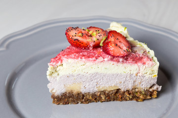 A slice of a raw vegan cake with strawberries and lime on a grey plate