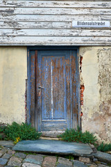 rotten door in a decayed house with flaked painting and cracked plaster on brick wall in old stavanger
